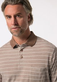 Hnědé a bílé pruhované polo tričko s hnědým límečkem, třemi knoflíky a kapsou na prsou. Texturovaná látka s ležérním designem.