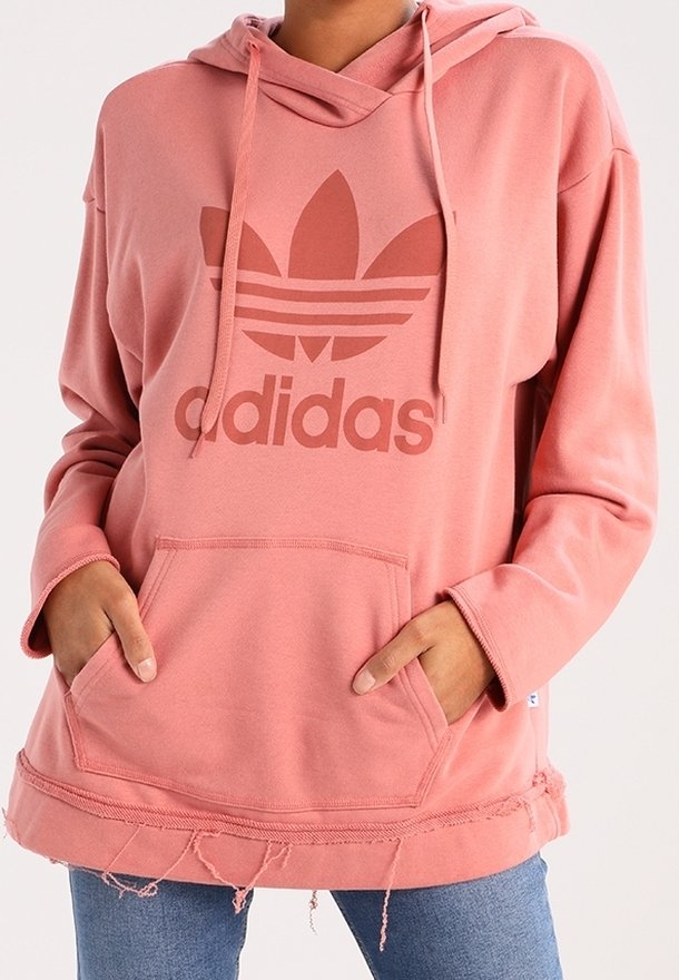 Růžová mikina Adidas s velkým logem, klokaní kapsou, kapucí na šňůrku a detailním zakončením s třásněmi. Vyrobena z měkkého a pohodlného materiálu.