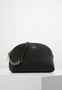 Černá taška přes rameno s zakřiveným tvarem, vyrobená z texturovaného materiálu. Obsahuje zlaté kovové prvky a řetízkový zdobný prvek na popruhu.