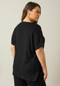 Sort kortærmet top lavet af struktureret stof, med rund halsudskæring, sideslidser og en afslappet pasform. Designet til komfort og bevægelsesfrihed.