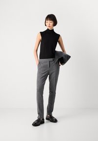 Svart ermeløs topp kombinert med grå, mønstrede high-waist bukser. Modellen holder en svart skinnclutch og har på seg svarte sko.