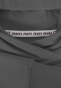 Szary materiał o miękkiej teksturze, z metką z napisem "Puchate Pluszowe Misie" na białym tle w kolorze czerwonym.