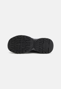 Black athletic shoe sole with textured rubber, featuring a wave pattern and grooves for traction. Circular logo near the heel.