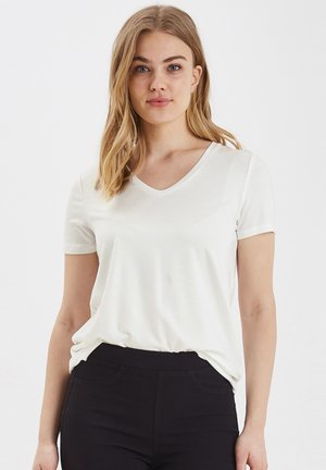 T-shirt bianca a maniche corte con scollo a V, realizzata in tessuto morbido, caratterizzata da una vestibilità rilassata e una texture liscia, abbinata a pantaloni neri.