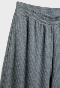 Sive prugaste hlače s elastičnim pojasom i naborima. Tkanina ima mekanu teksturu s suptilnim sjajem.