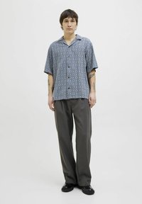 Camisa de manga corta, azul con un patrón de formas de diamante, combinada con pantalones oscuros grises y zapatos negros. Tejido de algodón, corte relajado.