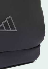 Svart ryggsäck med texturerat nylonmaterial, med en framträdande grå logotypdesign med tre ränder. Slät och hållbar tygfinish.