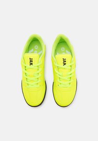 Scarpe da ginnastica giallo neon con tomaia sintetica liscia, lacci piatti, linguetta imbottita e suola nera a contrasto. Etichetta del marchio "JAK" visibile.