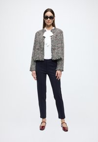 Jachetă din tweed cu tiv franjurat, bluză albă cu detaliu fundă, pantaloni bleumarin și pantofi plate burgundy cu vârful pătrat. Ochelari de soare negri cu ramă în formă de ochi de pisică.