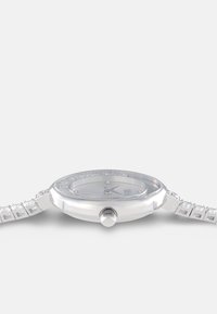 Silberne Uhr mit rundem Gehäuse, Kristallverzierungen um die Lünette und einem Gliederarmband mit quadratischen Details.