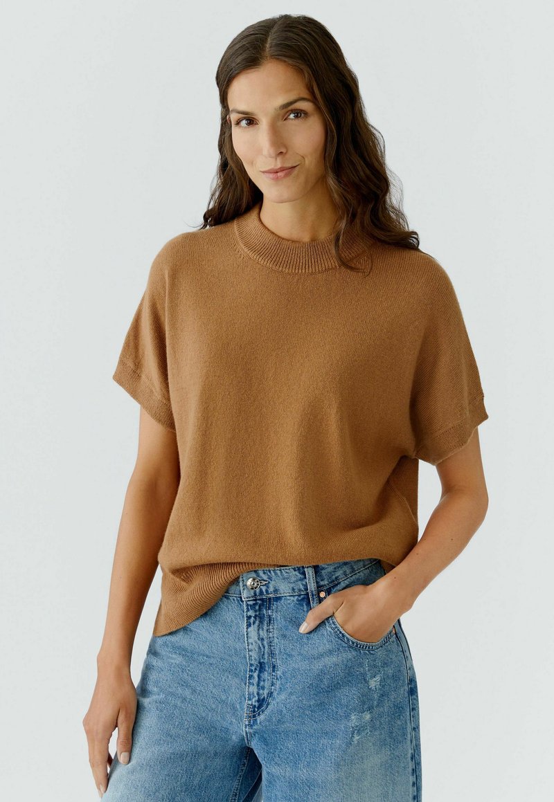 Bruin kortarmige gebreide trui met een ronde halslijn, gedragen over lichtblauwe high-waisted denim jeans. Gladde textuur, ontspannen pasvorm.