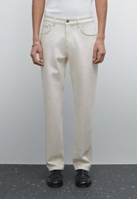 Pantaloni beige a gamba dritta realizzati in tessuto misto cotone, con tasche frontali, passanti per cintura e chiusura con un'unica bottone.