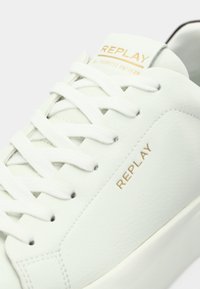 Λευκό δερμάτινο αθλητικό παπούτσι με ομαλή υφή, με επίπεδα λευκά κορδόνια και χρυσό λογότυπο "REPLAY" στη γλώσσα, κομψό σχεδιασμό και ελάχιστες λεπτομέρειες.