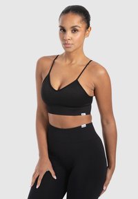 Zwarte geribbelde crop top met dunne verstelbare bandjes, voorzien van een V-halslijn en een merklabel op de taille. Gecombineerd met hoge zwarte leggings.