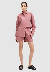 Camisa de algodón rosa con cuello puntiagudo, mangas largas y botones en el frente, combinada con pantalones cortos a juego que tienen una cinturilla elástica.
