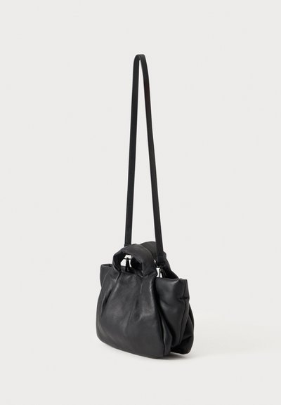 Sac à main souple en cuir noir avec des poignées courtes et une longue bandoulière sur un fond clair uni.