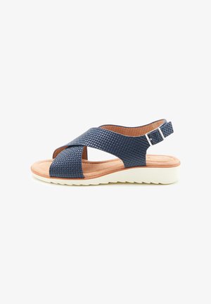 Sandal in tessuto blu navy con cinturini incrociati, dotata di una cinghia alla caviglia con fibbia, soletta imbottita beige e suola bianca testurizzata.