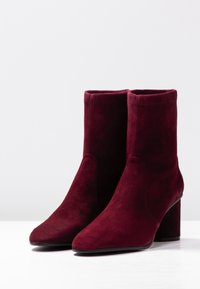 Botines de ante burdeos con punta afilada y tacón bloque de 3,5 pulgadas, que presentan una textura suave y un diseño minimalista.