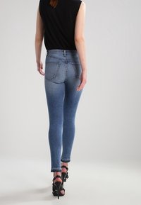 Jeans de mezclilla azul de tiro alto y ajustados, con bolsillos traseros, dobladillo sin terminar y un ligero desvanecimiento. Combinados con una blusa negra sin mangas y tacones.