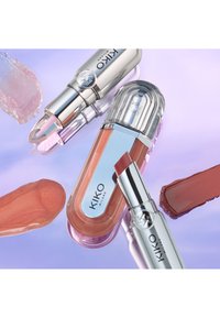 KIKO Milano Lippenstifte und Lipgloss mit silbernen Hüllen und nude-rosafarbenen Nuancen, dargestellt mit passenden Farbflecken auf pastell-lila Hintergrund.