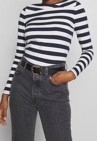 Marinblå och vit randig långärmad topp i kombination med högmidjade svarta jeans. Outfiten fulländas med ett svart bälte med ett guldspänne.