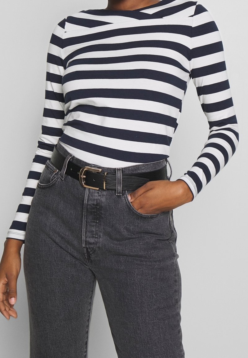 Marinblå och vit randig långärmad topp i kombination med högmidjade svarta jeans. Outfiten fulländas med ett svart bälte med ett guldspänne.