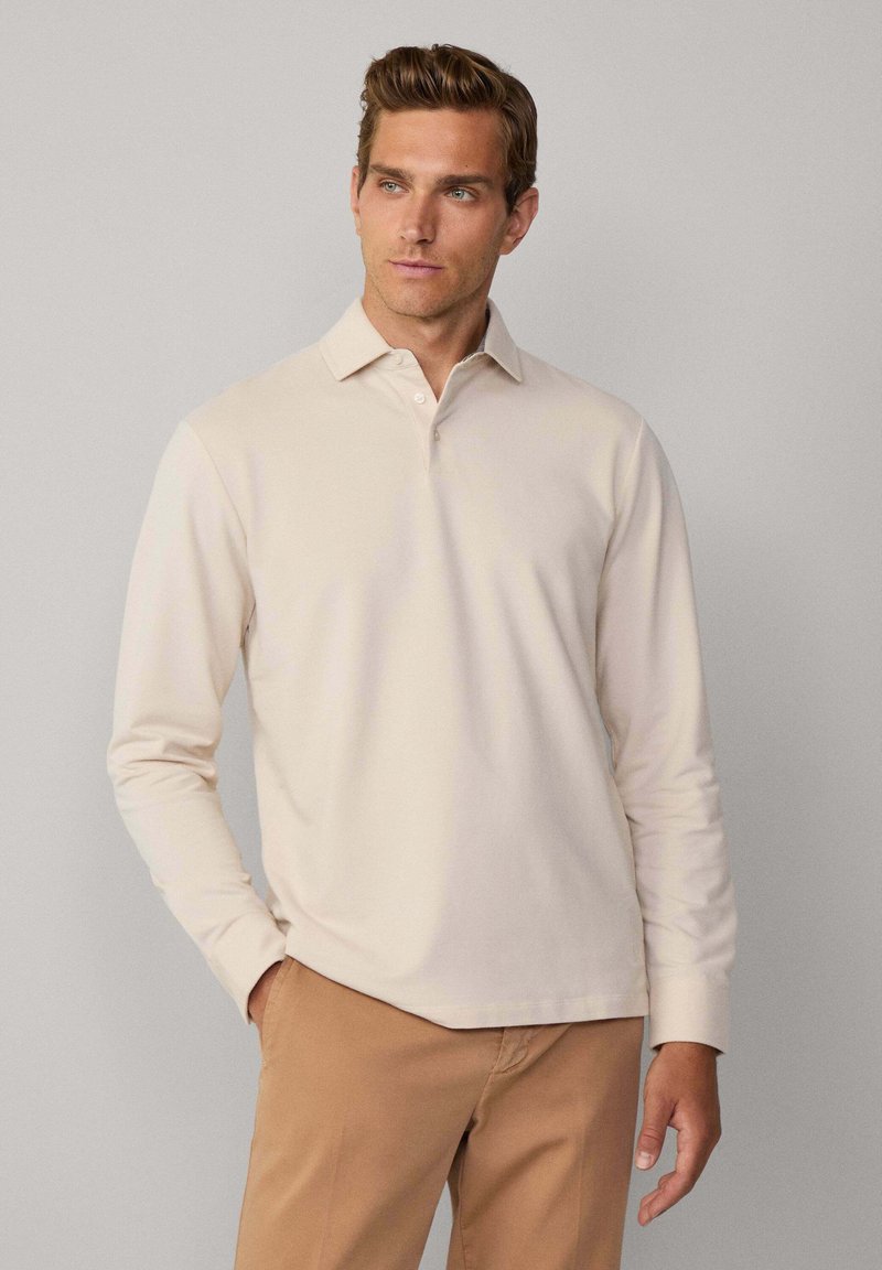 Långärmad polo i ljusbeige bomull, med en klassisk krage och treknapplås, tillsammans med ljusbruna byxor.