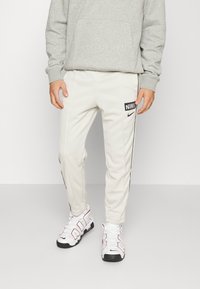 Nike ljusgrå joggers med svarta sidodetaljer och logotyp, kombinerade med vita sneakers med röda och svarta detaljer.