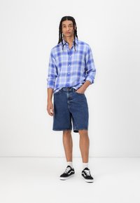 Blue checkered button-up shirt, denim shorts, and black sneakers with white soles. Casual outfit displayed against a plain background.