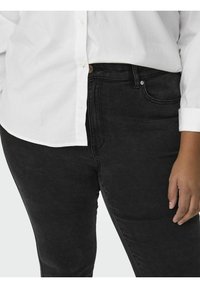 Black denim jeans with a smooth texture, featuring a high waist, front pocket, and a subtle faded pattern. Paired with a white button-up shirt.