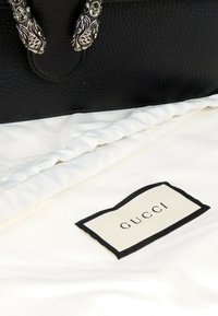 Gros plan d'un sac en cuir noir texturé avec des ornements en tête d'animal argentés posé sur un tissu blanc portant l'étiquette Gucci.