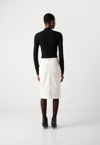 Zwarte nauwsluitende sweater, witte spijkerrok tot op de knie met achterzakken, zichtbare stiksels en zwarte enkellaarsjes. Glad textuur en casual ontwerp.