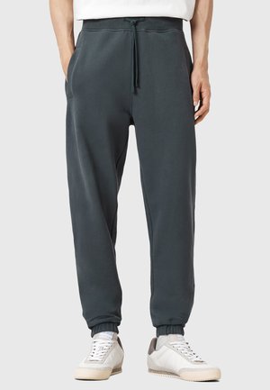Dark gray sweatpants with elastic cuffs and a drawstring waistband, featuring side pockets and a soft, textured fabric. Worn with white sneakers.