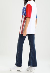 T-shirt a maniche corte con design della bandiera americana nei colori rosso, bianco e blu; abbinato a jeans svasati scuri con dettagli a bottone.