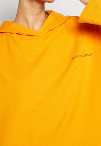 Felpa gialla con tasca a marsupio e cappuccio con cordino. Presenta il testo "MARCO'POLODENIM" in un colore a contrasto sul petto.