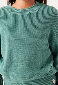 Sweter z dzianiny w kolorze turkusowym, z prążkowaną fakturą, okrągłym dekoltem i akcentami przy dolnym brzegu. Wykonany z miękkiej mieszanki tkanin.