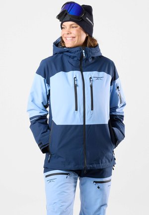 Blue ski jacket with a lighter blue upper panel, two chest pockets, adjustable hood, and a matching ski pant. Features zippers and accents.