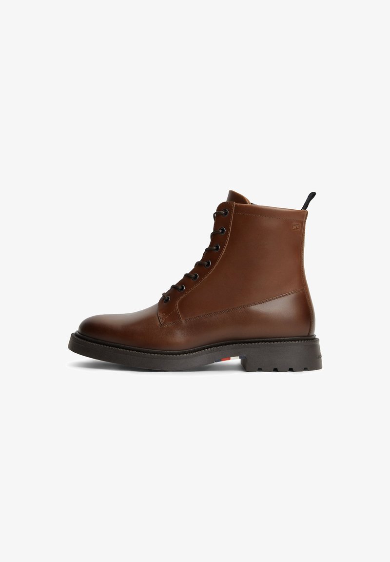 Καφέ δερμάτινο μποτάκι με κορδόνια, μαύρη ταινία για τράβηγμα και μαύρη σόλα με βαθύ πέλμα και μικρές κόκκινες, λευκές και μπλε λεπτομέρειες.