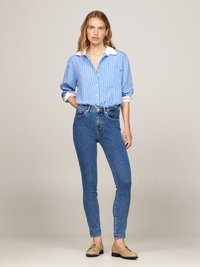 Camisa de botones a rayas azules con cuello blanco, combinada con jeans skinny azules y zapatos de tela beige. Diseño sencillo, corte holgado.