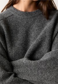 Pull en laine gris avec un col rond côtelé, doté d'une texture douce et d'épaules tombantes. Design chaud et confortable.