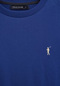 Maglietta blu a girocollo con piccolo logo ricamato beige di un giocatore di polo sul petto a sinistra e etichetta "POLO CLUB" all'interno del colletto.