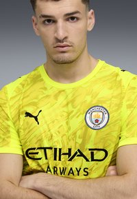 Gul fotbollströja med en texturerad mönstring, med svart Puma-logotyp, texten "ETIHAD AIRWAYS" och Manchester Citys emblem.