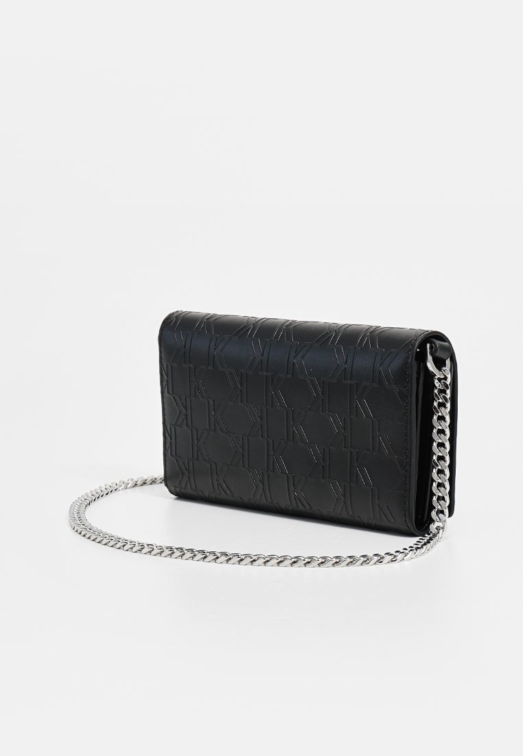 Sac à main en cuir noir avec motif de logo gaufré, bandoulière en chaîne et forme rectangulaire. Texture lisse avec des accents métalliques.
