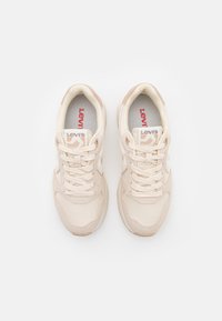 Beige sneakers with a mesh and suede upper, white accents, round toe, and a rubber sole. Features logo on the tongue and patterned lace.