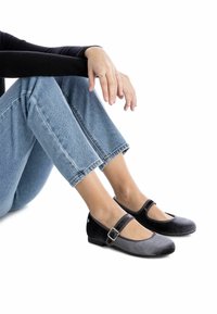 Bailarinas de ante negras y grises con punta cerrada, tira en el tobillo y detalle de hebilla. Las lleva puestas con unos jeans cropped de color azul claro.