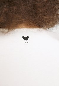 T-shirt blanc avec un logo papillon noir et "WM" imprimé sur la nuque au dos. Tissu doux et lisse avec un col ras du cou standard.