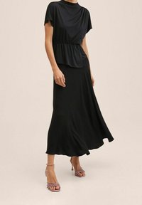 Blusa negra con una cintura ajustada y mangas cortas, combinada con una falda negra fluida. El calzado presenta sandalias de tacón con tiras en color rosa.