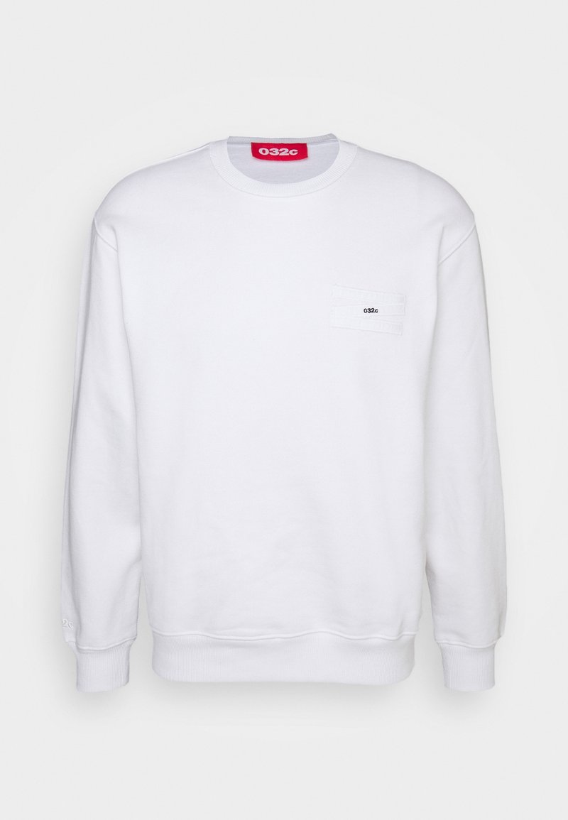 Sweatshirt blanc à manches longues avec encolure ronde, petite poche sur la poitrine portant l'étiquette "032c" et une étiquette rouge "032c" à l'intérieur du col.