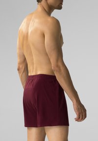 Męskie bordowe bokserki z elastycznym pasem, wykonane z gładkiego materiału, o długości powyżej kolana, bez widocznych wzorów ani elementów metalowych.