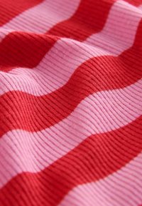 Pruhovaná tkanina s prekladanými vlnitými vzormi v červenej a ružovej farbe. Textúra je žebernatá, čo jej dodáva hmatový charakter.